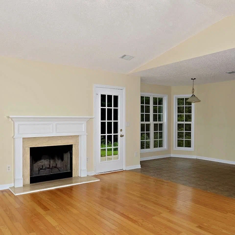 Empty living room with hardwood floors, white fireplace, and French doors leading to a bright corner area