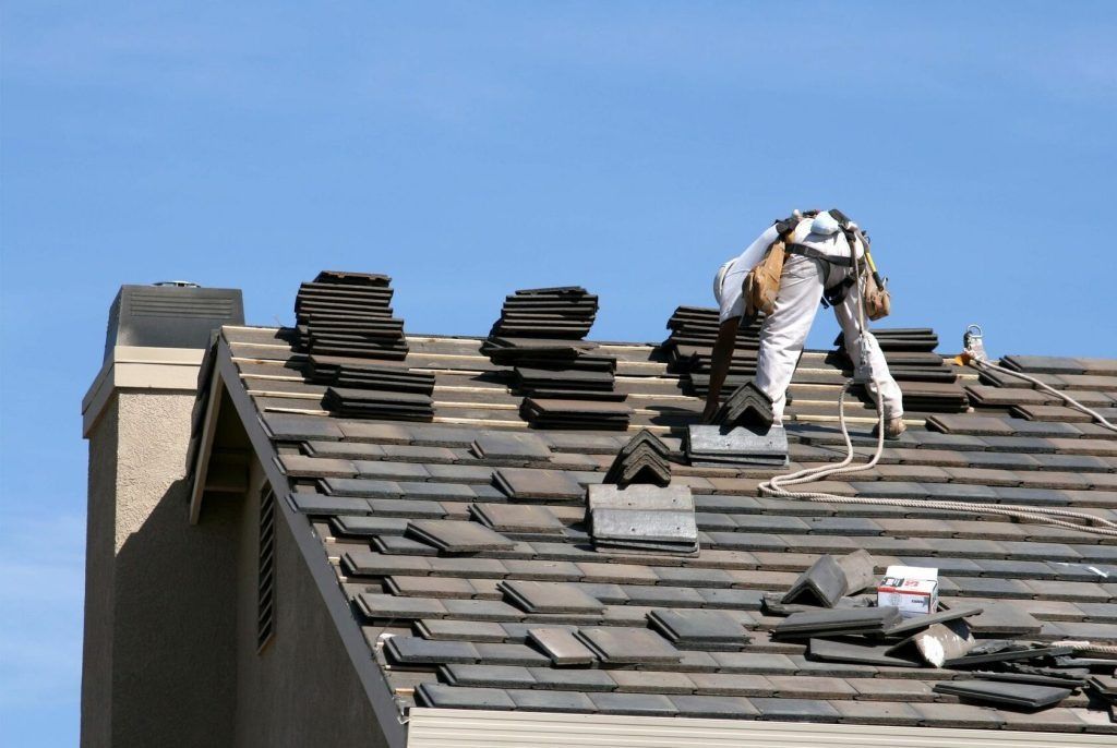 Worker repairing gray shingle roof under blue sky