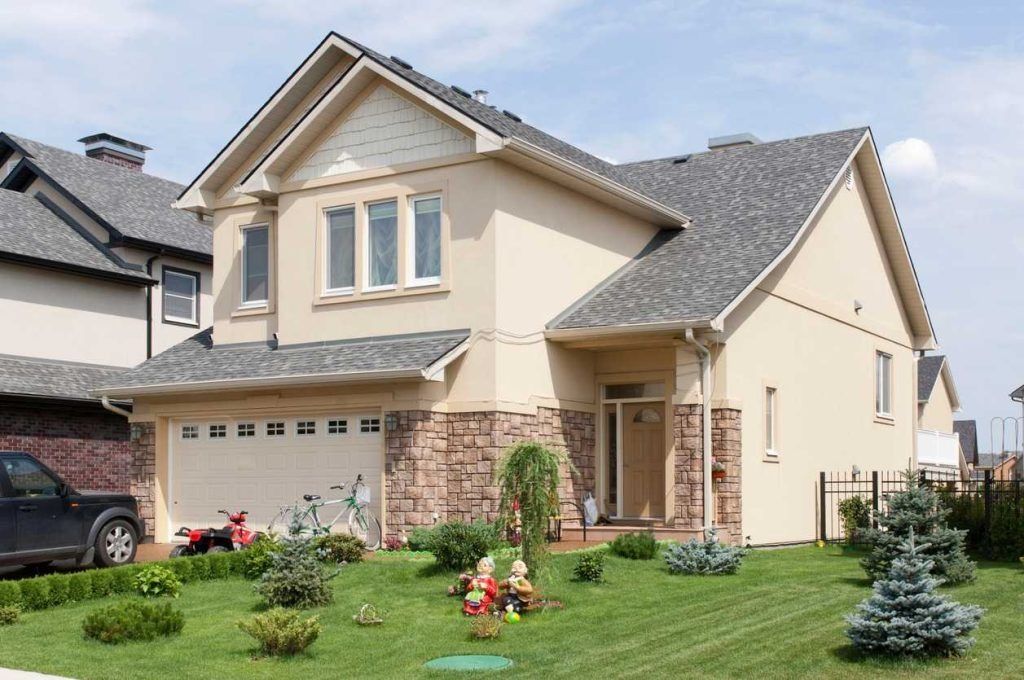 Two-story beige suburban house with stone accents, a front lawn, and a small garden