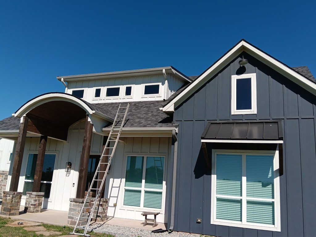 Modern gray house exterior with arched entry, white trim, and large windows under a clear blue sky