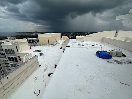 Storm clouds over a flat white rooftop with rooftop equipment and blue tarps.