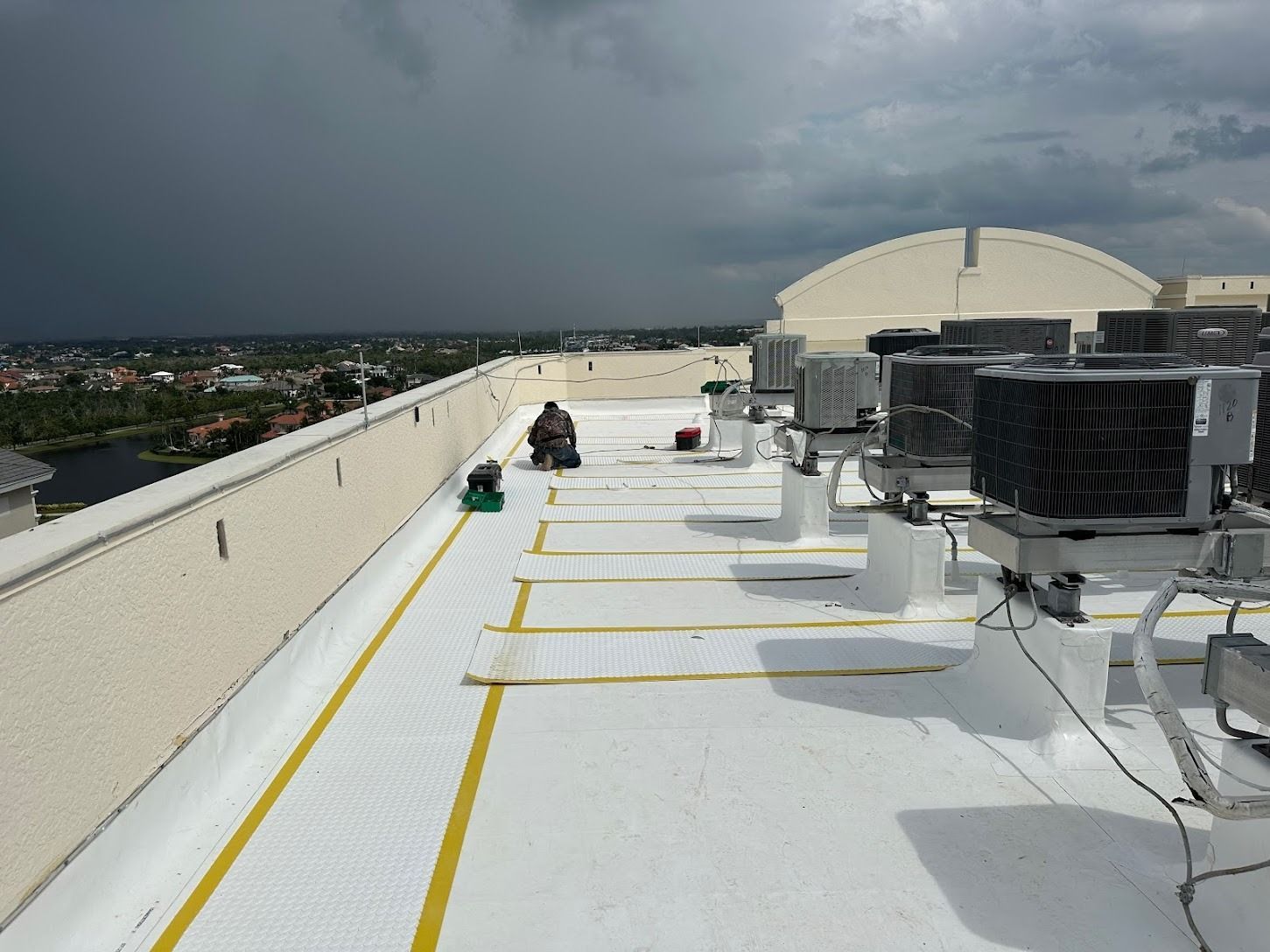 Rooftop with white roofing, HVAC units, and a stormy sky over distant cityscape