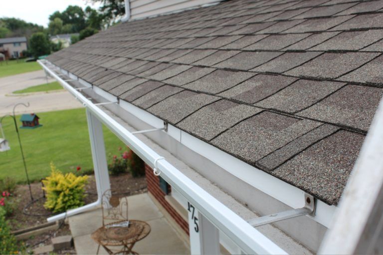 White gutter mounted along the edge of a shingled roof beside a house porch