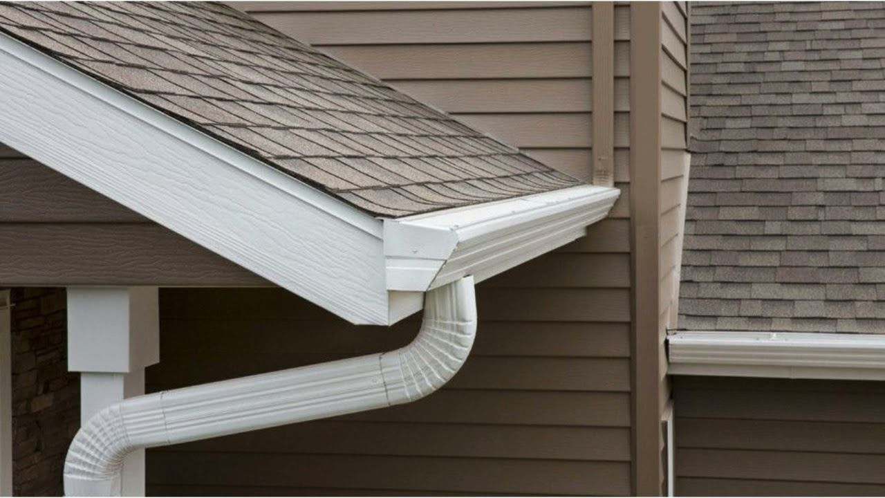 White gutter and downspout on a tan house roof corner