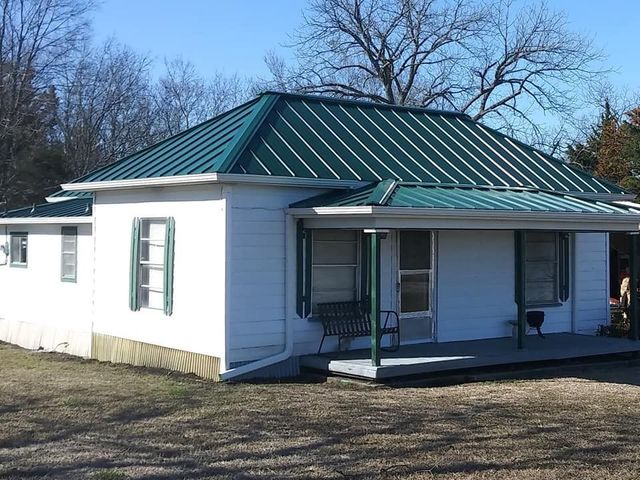 Small white house with a green metal roof and front porch, set in a grassy yard with bare trees.