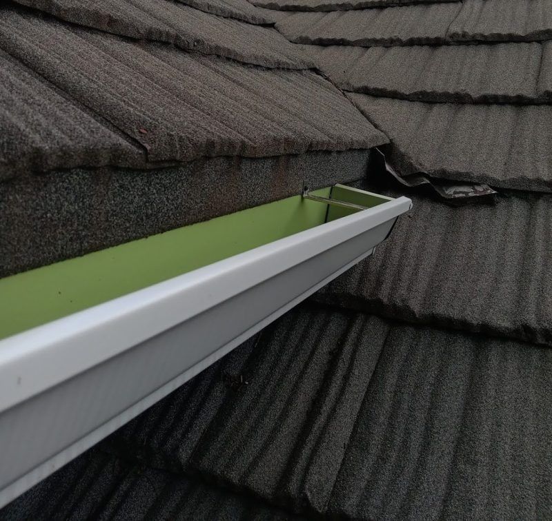 White gutter on gray shingle roof with green water pooling inside