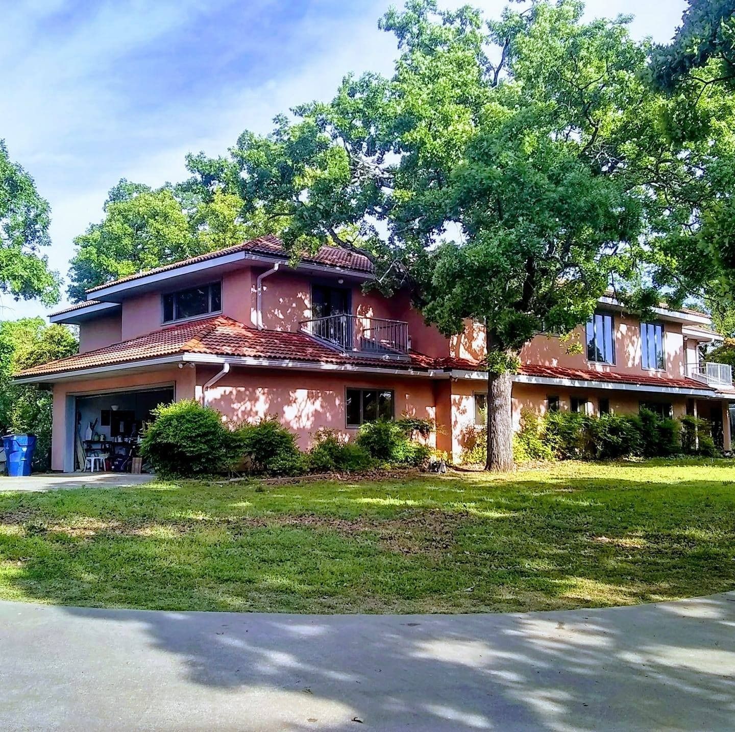 Two-story brick house with red roof and large trees in front, viewed from the street