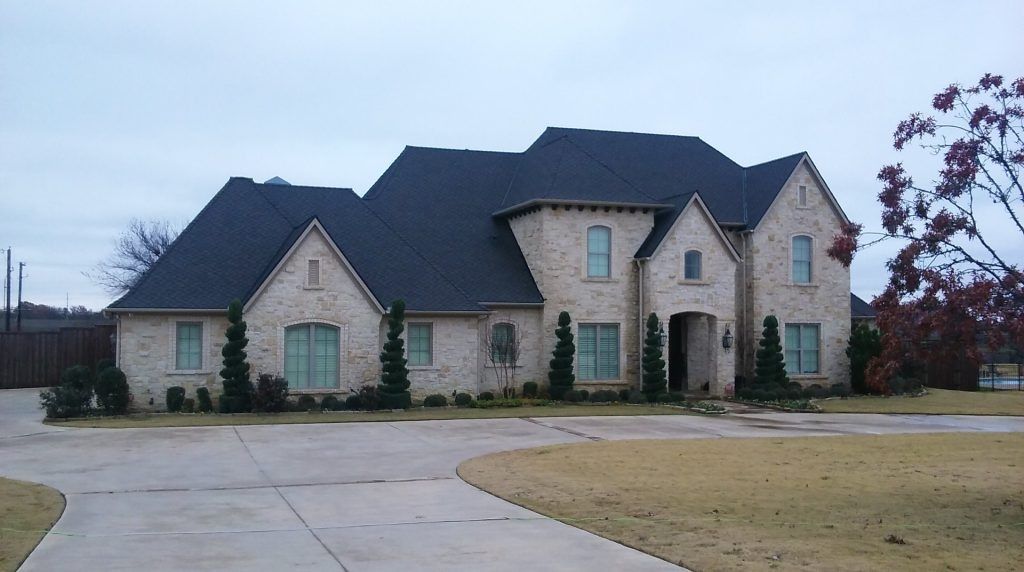 Large beige suburban house with dark roof and curved driveway on an overcast day