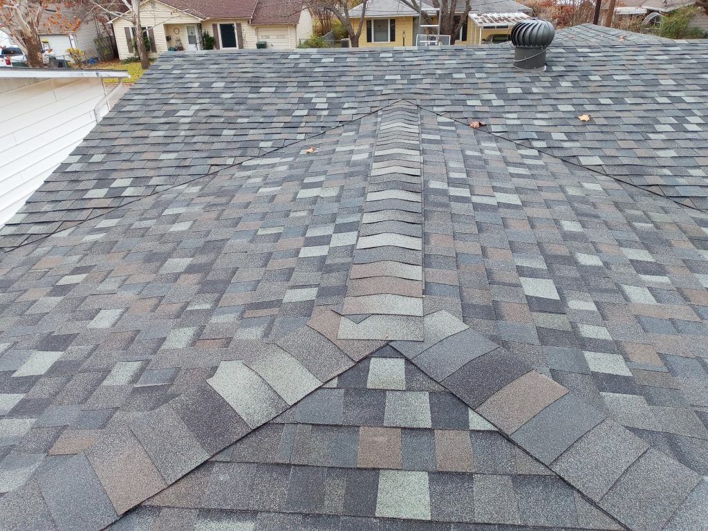 Residential shingle roof with patchwork repairs and a ridge vent, viewed from above