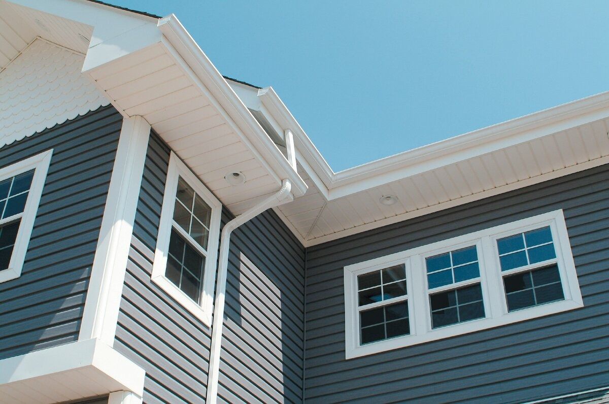 Blue-gray house exterior with white-trimmed windows and roof eaves against a clear blue sky