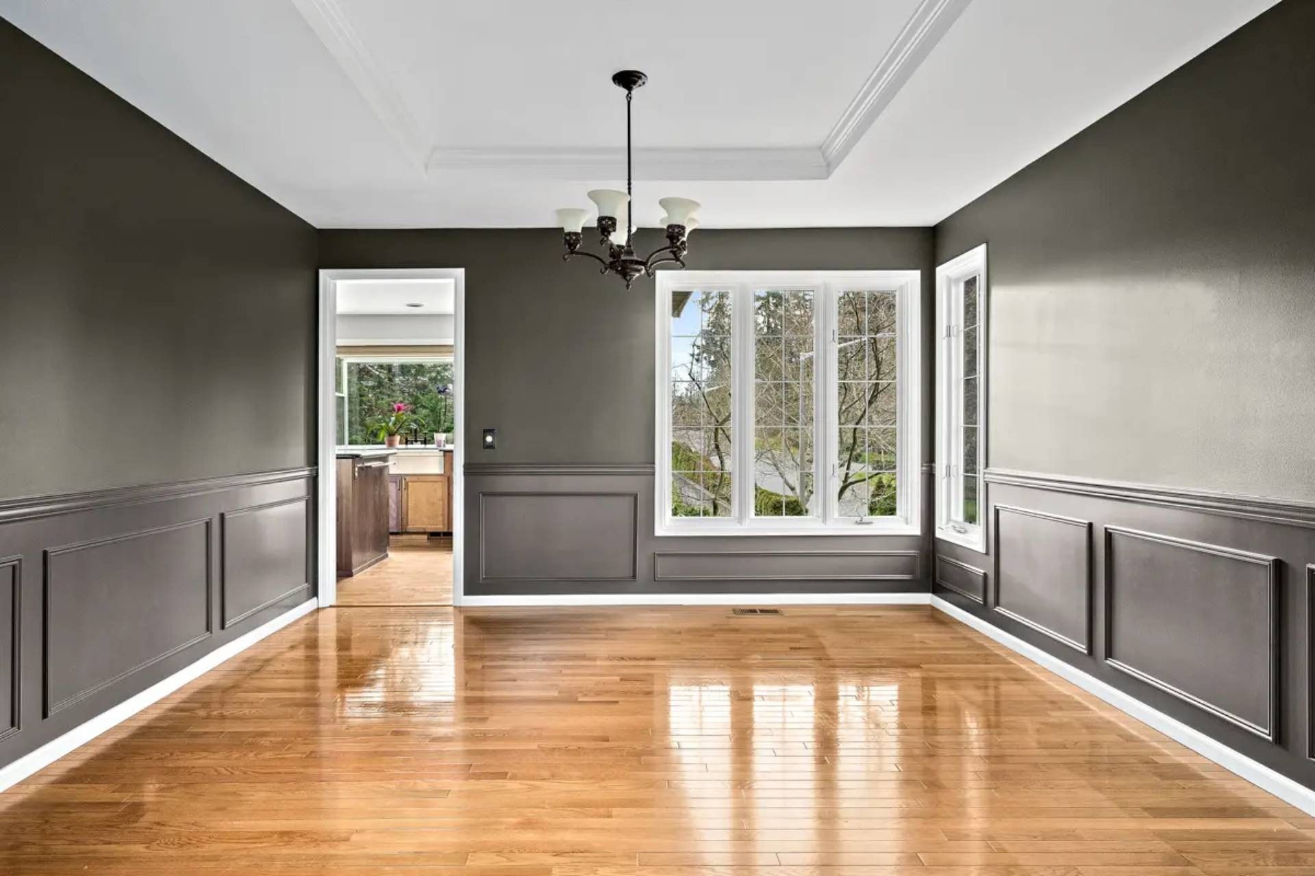 Empty dining room with dark gray wainscoting, hardwood floors, and large windows letting in natural light