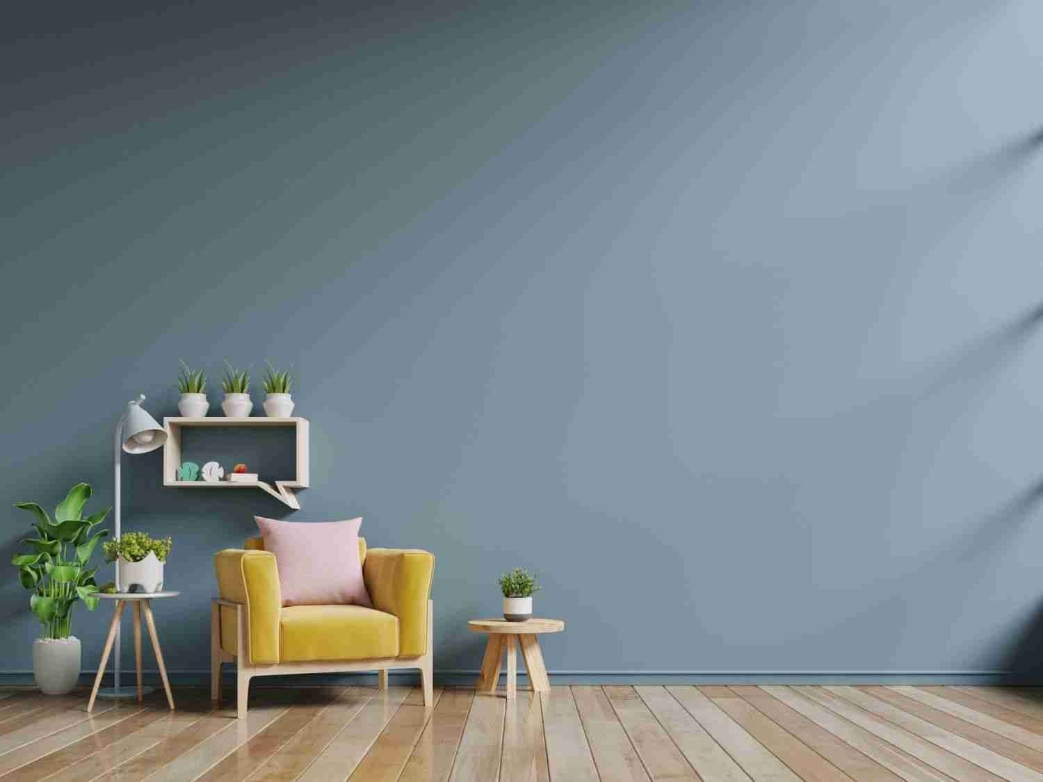 Modern living room with a mustard armchair, wall shelf, potted plants, and a small wooden table against a blue wall