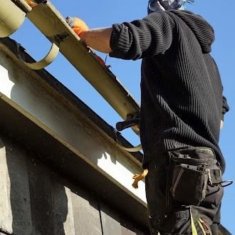Worker on a roof installing a yellow beam against a blue sky.