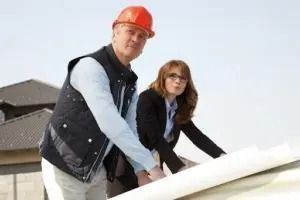 Two workers in hard hats lifting a white roofing panel on a rooftop