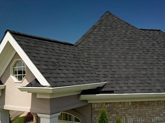 Two dark gray shingled roof peaks on a beige house against a blue sky