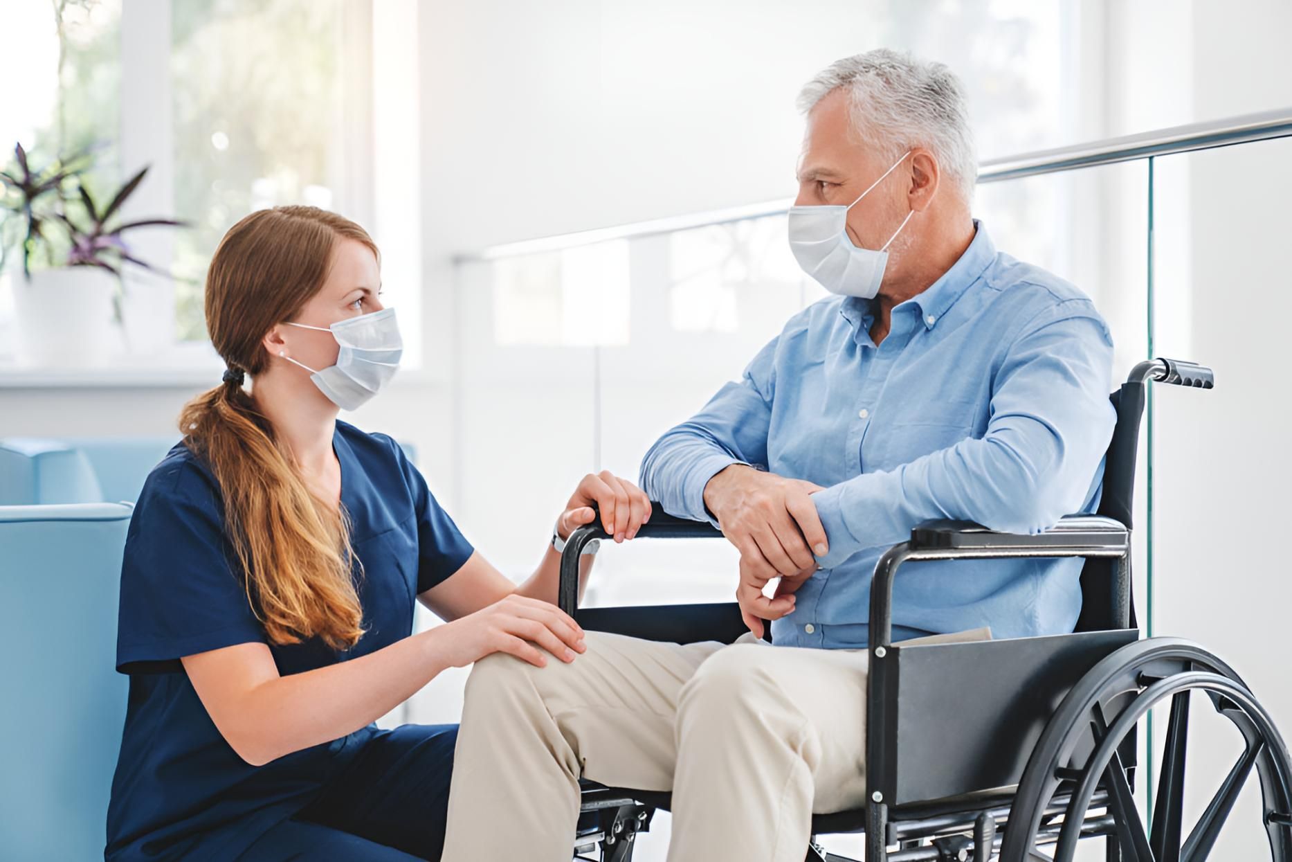 A Nurse Wearing a Mask is Talking to an Elderly Man in a Wheelchair — Active Lifestyle Supports In Kiama, NSW