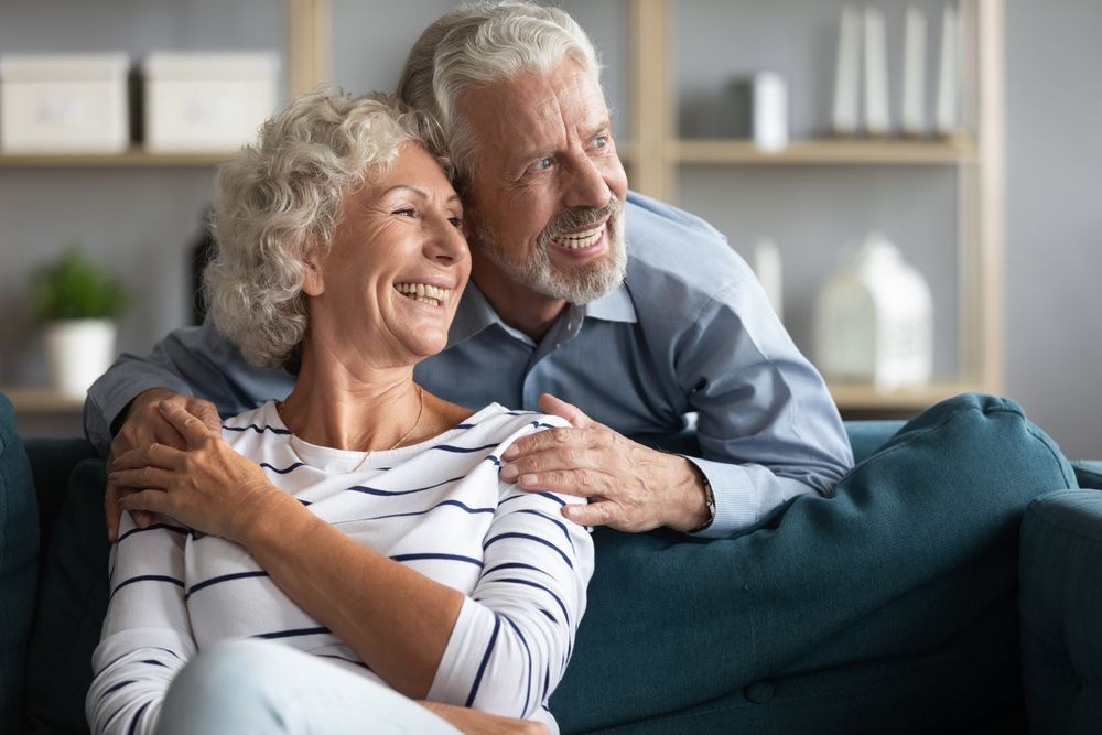 An Elderly Couple is Sitting on a Couch and Hugging Each Other — Active Lifestyle Supports In Tullimbar, NSW