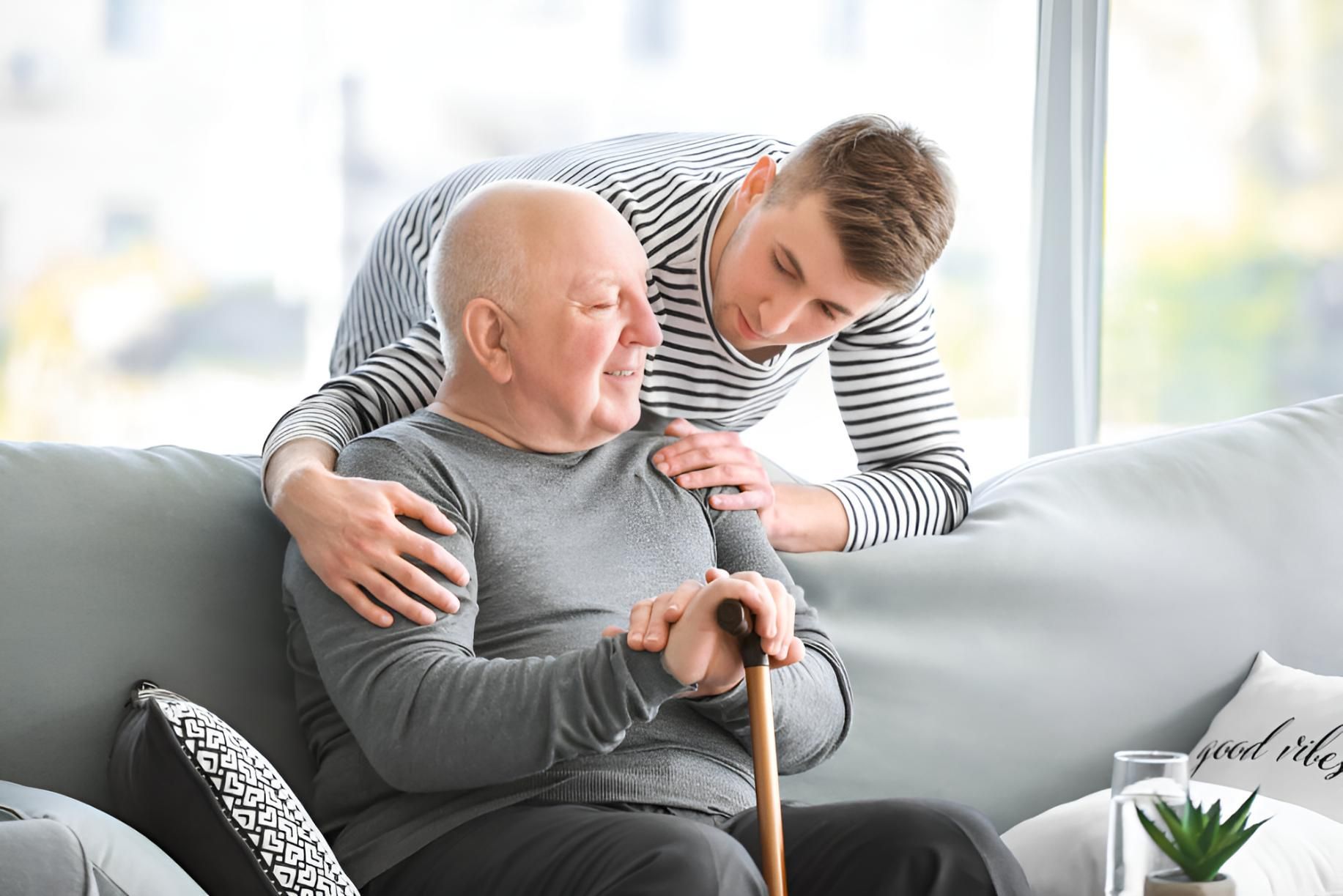 An Elderly Man With a Cane is Sitting on a Couch With a Young Man — Active Lifestyle Supports In Kiama, NSW