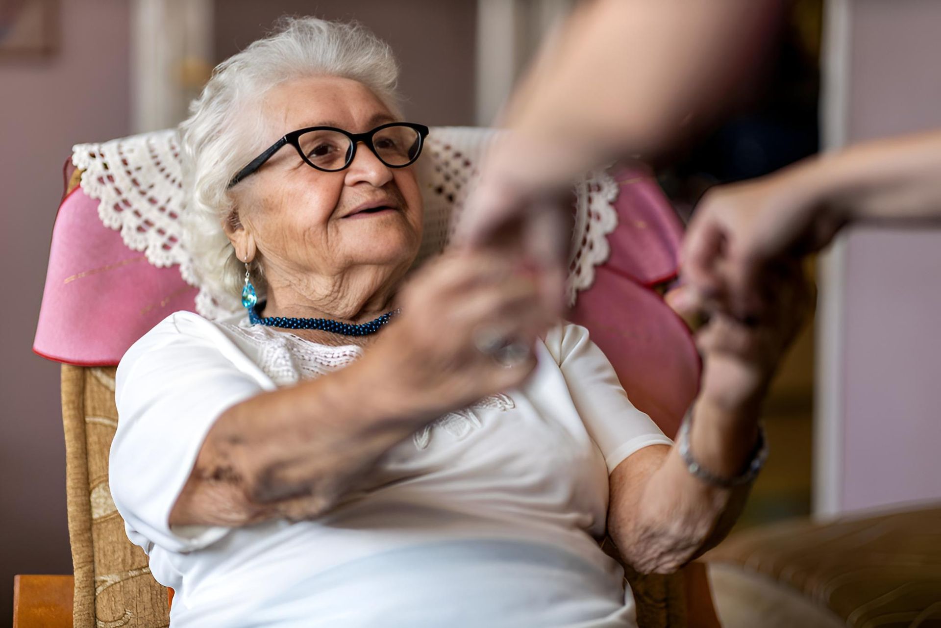 An Elderly Woman is Sitting in a Chair Holding a Person's Hand — Active Lifestyle Supports In Tullimbar, NSW
