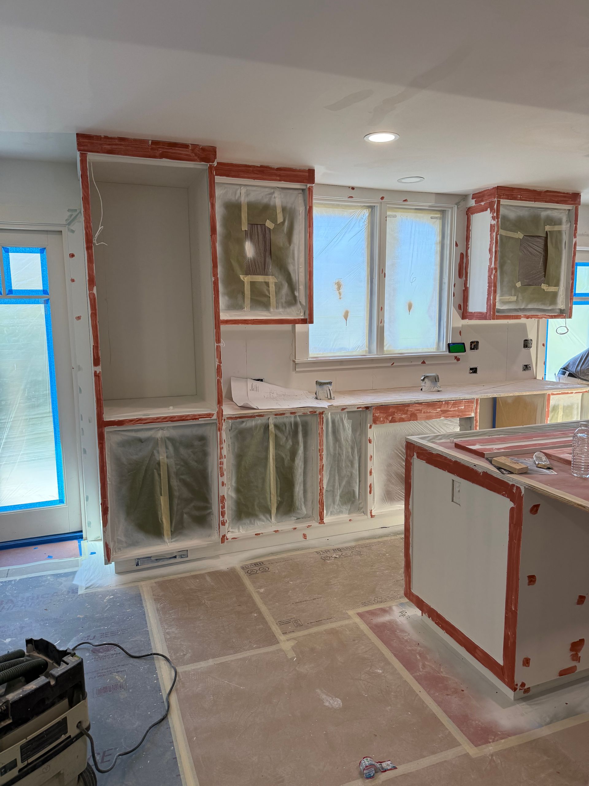 A room under renovation with wooden ceiling beams, drywall patches, ladders, and scaffolding on a hardwood floor.