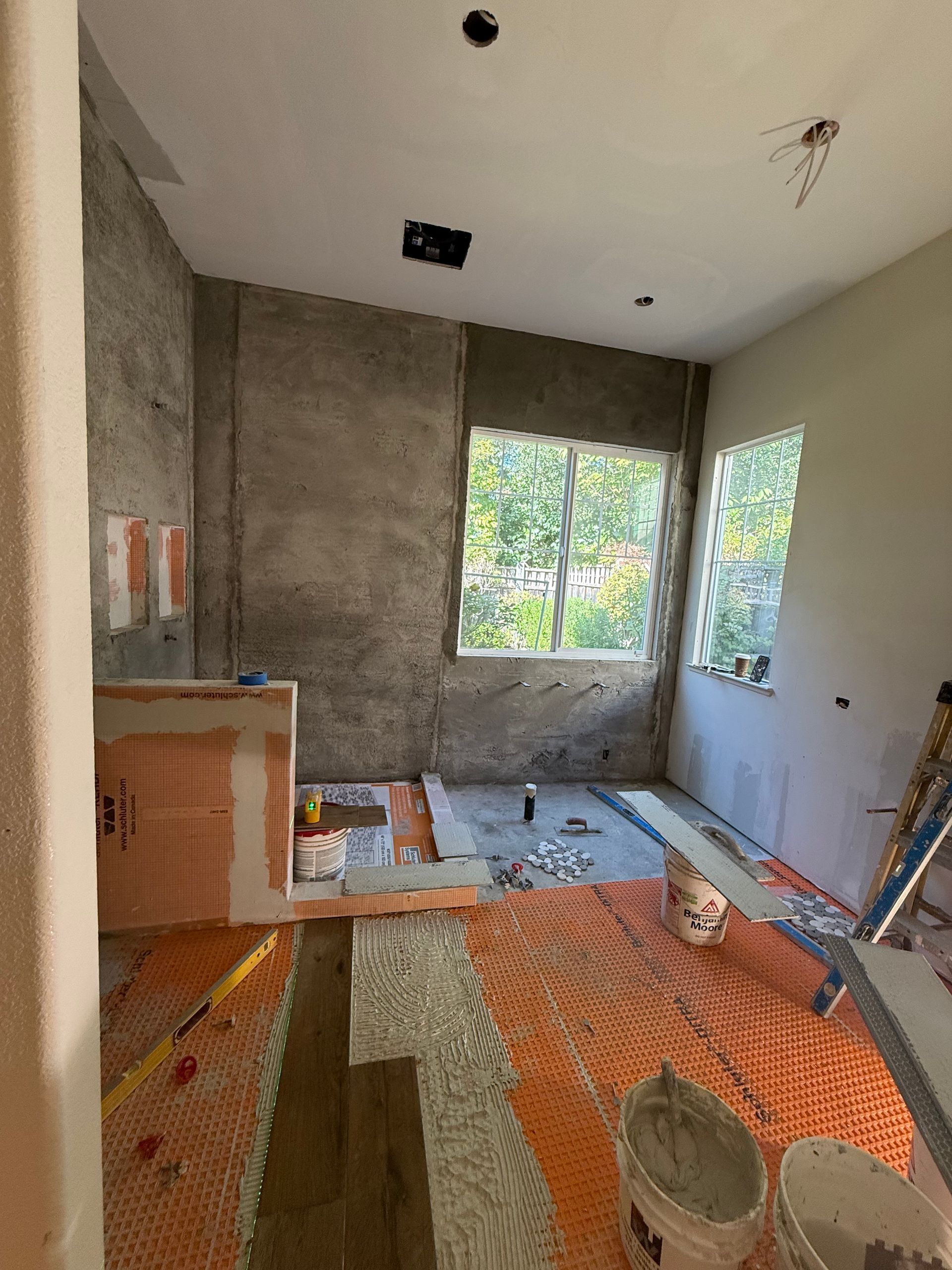 A room under construction featuring an orange waterproof floor membrane, unfinished walls, and a shower curb installation.