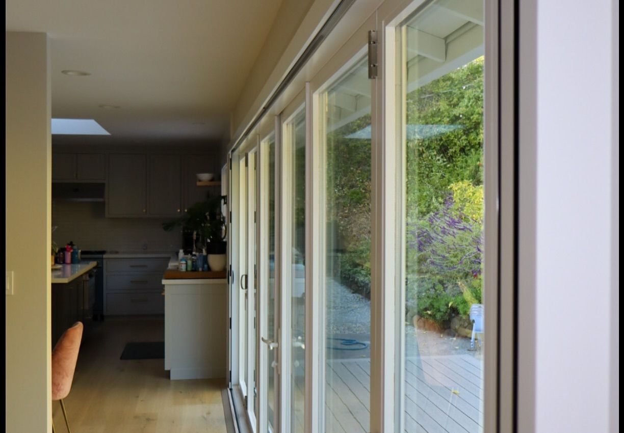 A view from inside a modern kitchen looking through a large set of glass bifold doors opening onto a sunny garden deck.