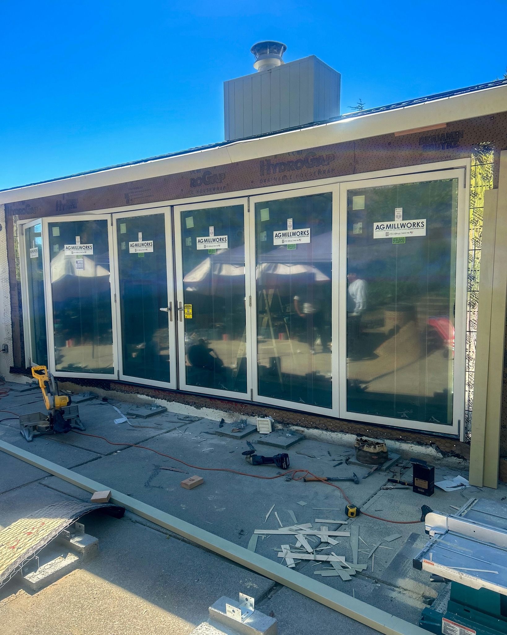 Newly installed white-framed folding glass doors on a house patio under construction with tools on the ground.