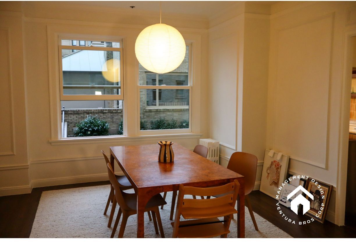 A wooden dining table with four chairs sits on a white rug under a large, glowing spherical pendant light.