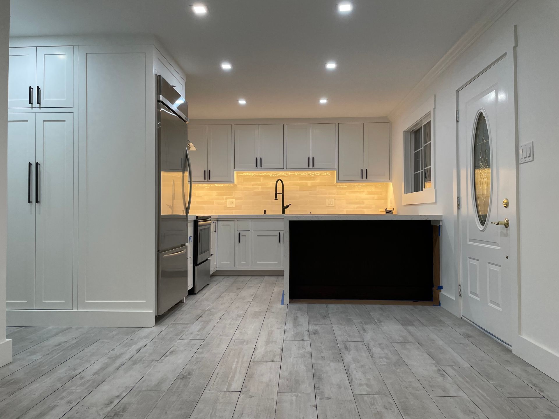 Bright modern kitchen with white cabinets, gray flooring, black island, and recessed ceiling lights