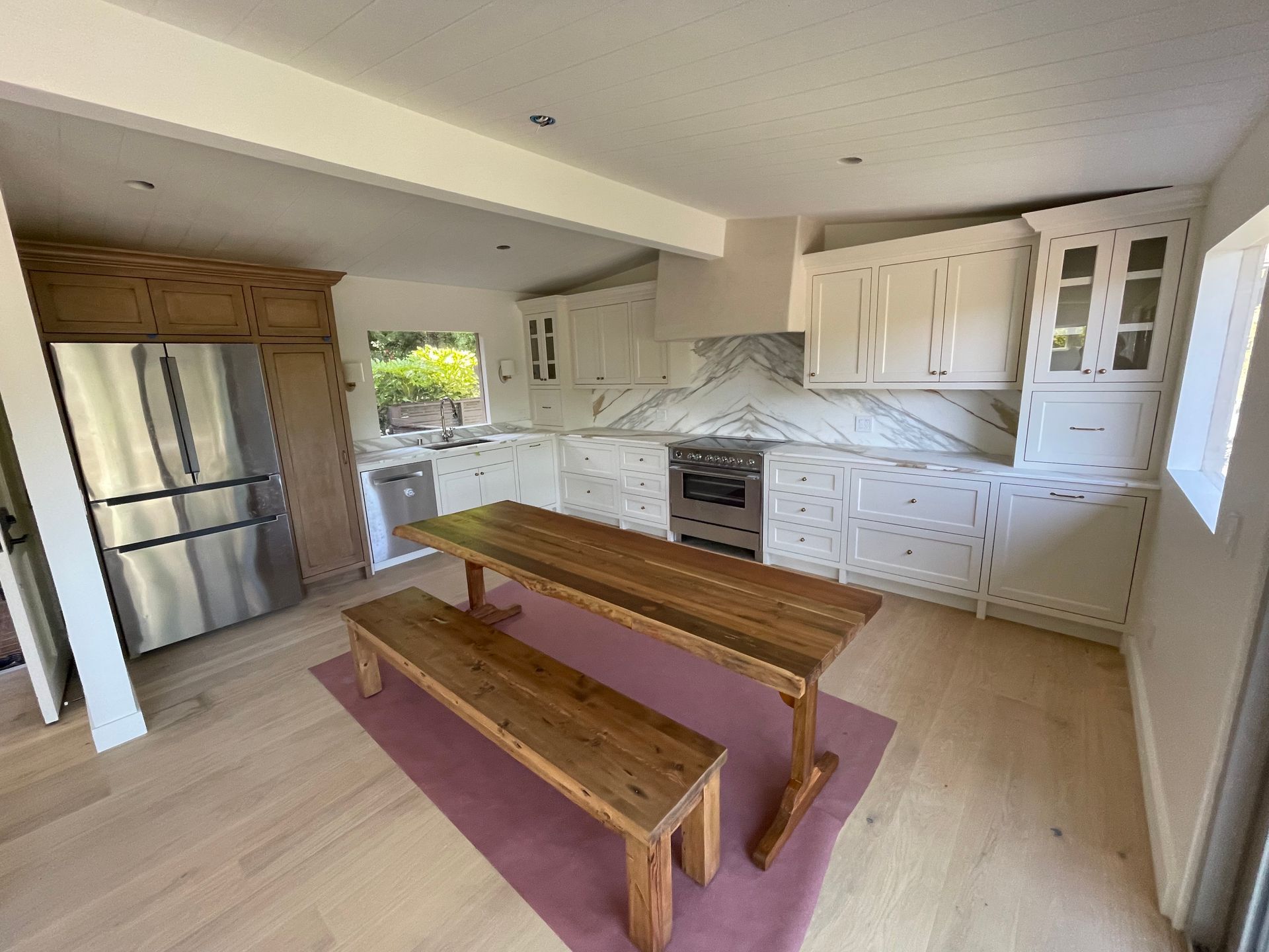 Bright kitchen with white cabinets, stainless fridge, island table, and bench seating.