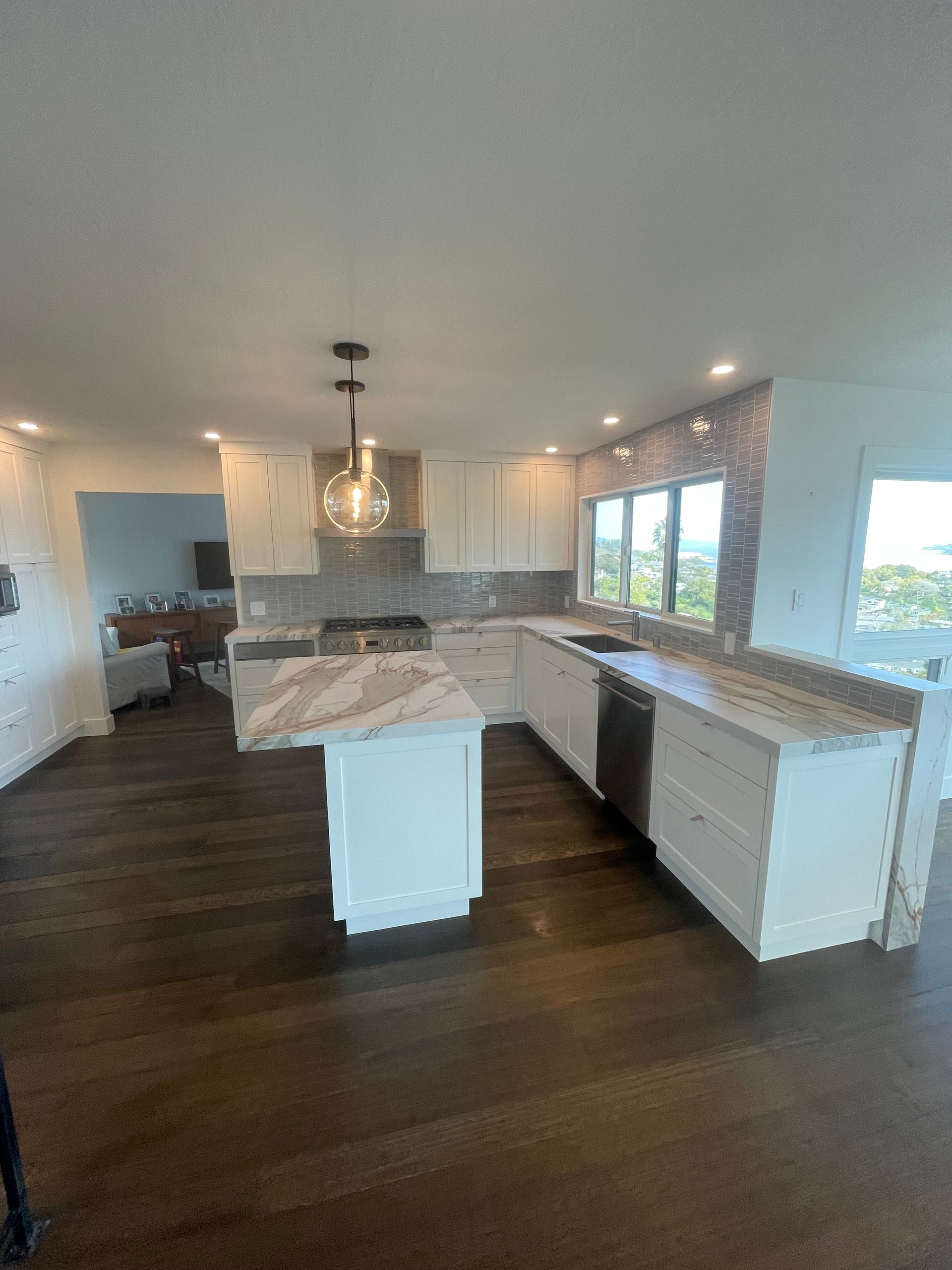 Bright modern kitchen with white cabinets, large island, dark wood floor, and windows along the right wall