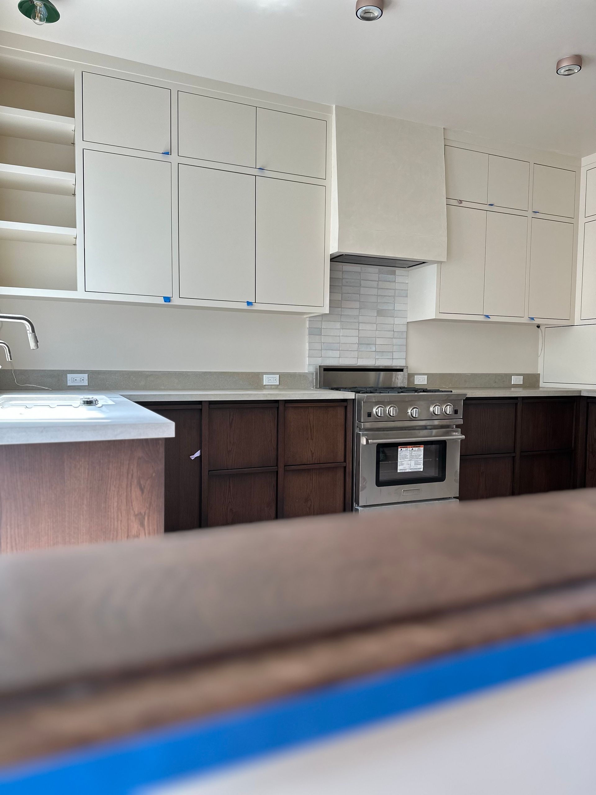 Empty kitchen with white cabinets, dark lower cabinets, a stove, and a tiled backsplash under renovation.