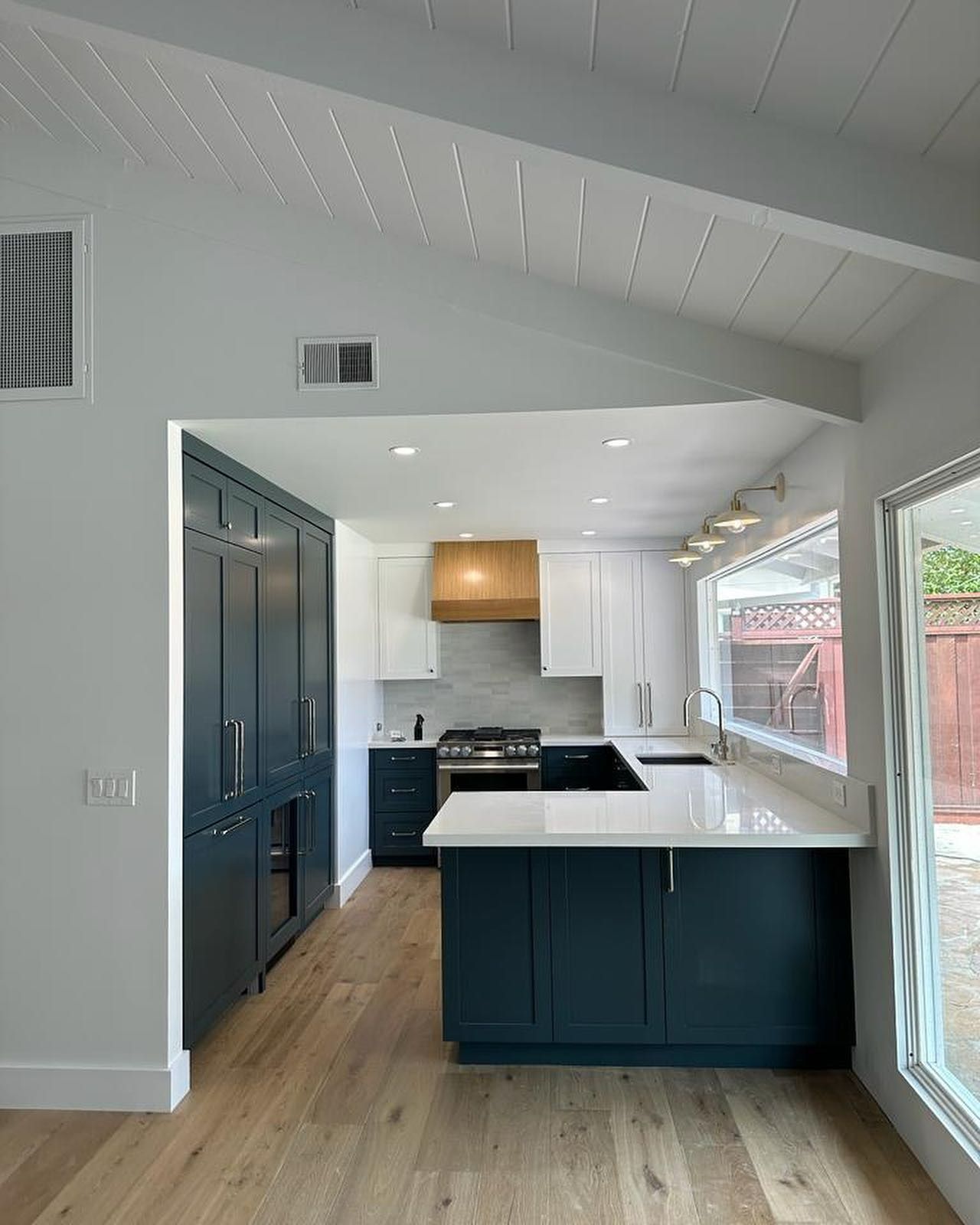 Modern kitchen with navy cabinets, white island, skylight ceiling, and large windows.
