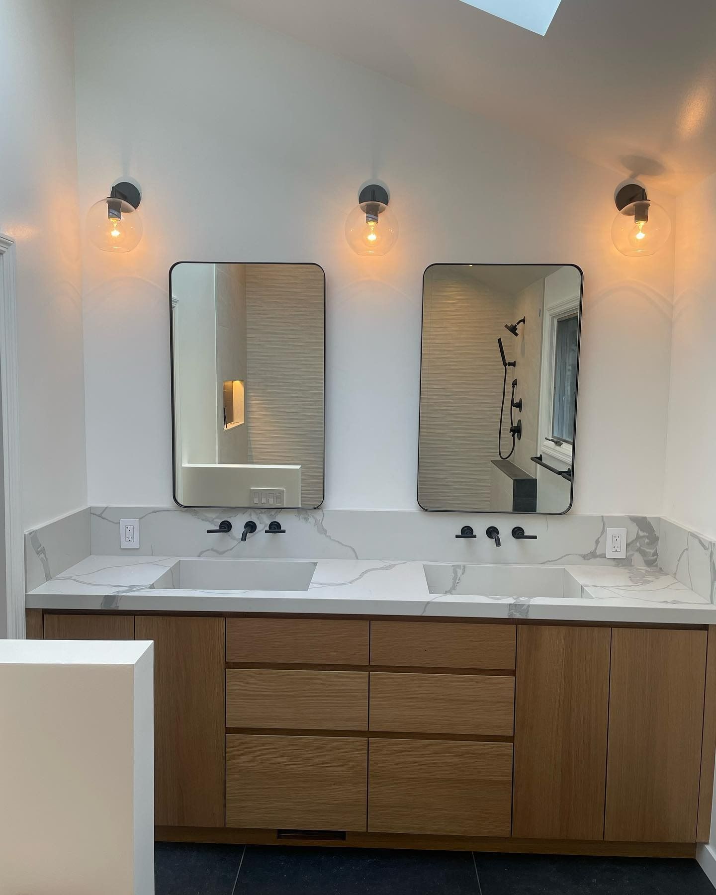 Modern bathroom vanity with double sinks, two mirrors, and warm wall sconces above a wood cabinet.
