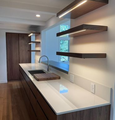A modern kitchen with dark wood cabinets, white countertops, and three floating shelves with built-in LED lighting.