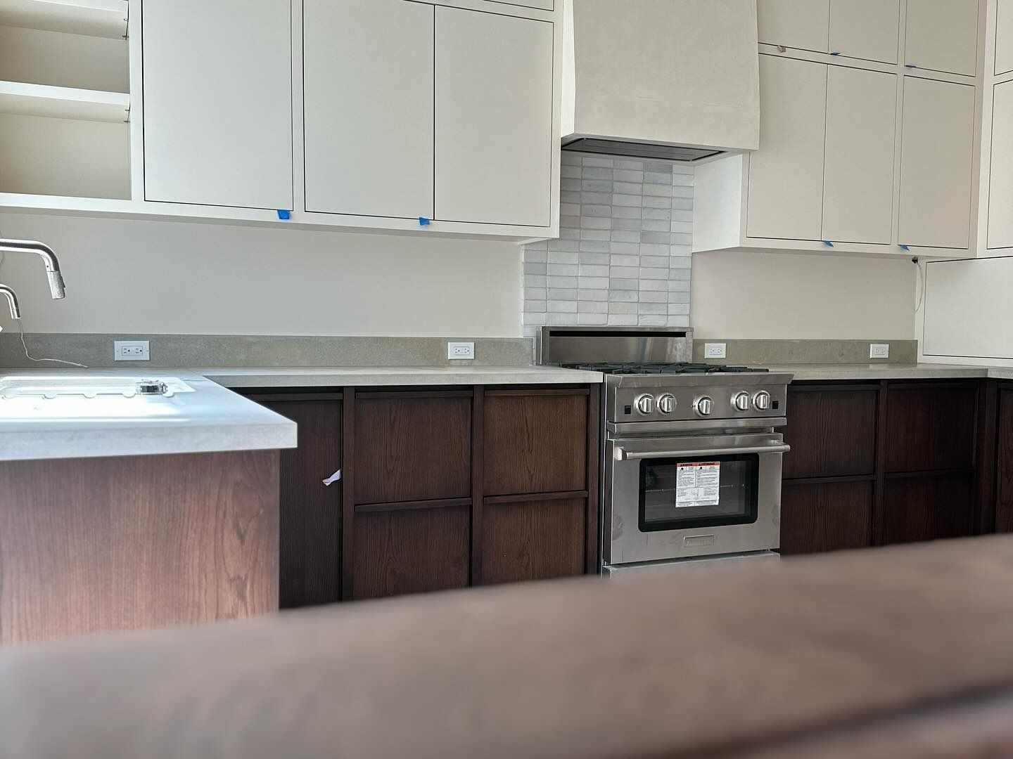 A kitchen with white upper cabinets, dark wood lower cabinets, light countertops, and a stainless steel oven.