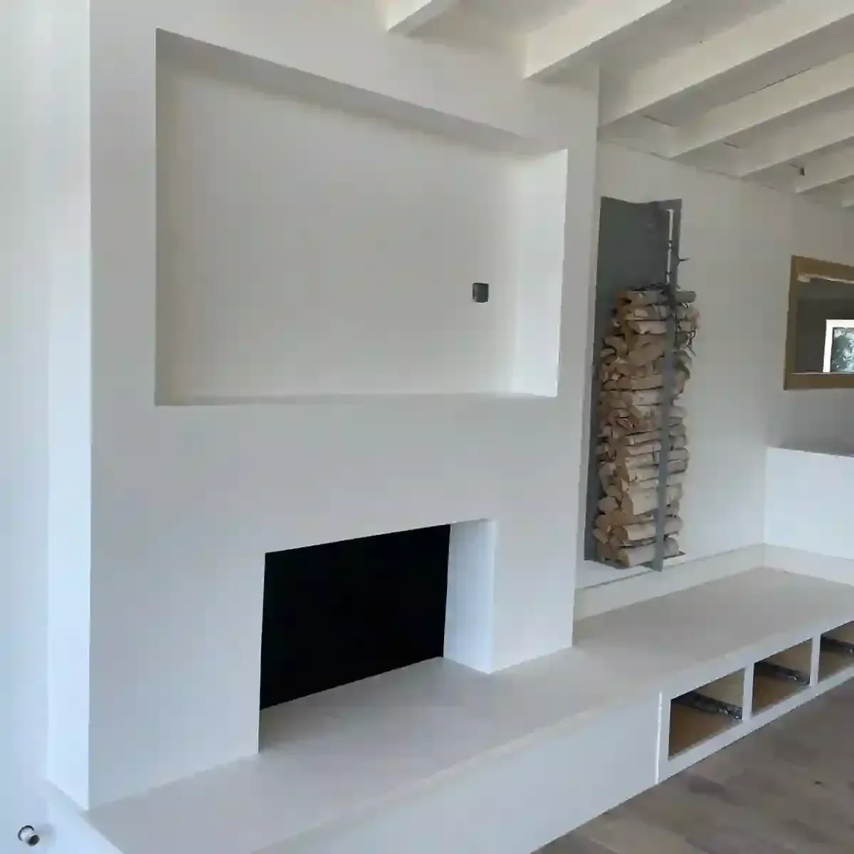 A white fireplace feature wall with a recessed TV niche, a hearth with built-in storage, and a vertical wood rack.