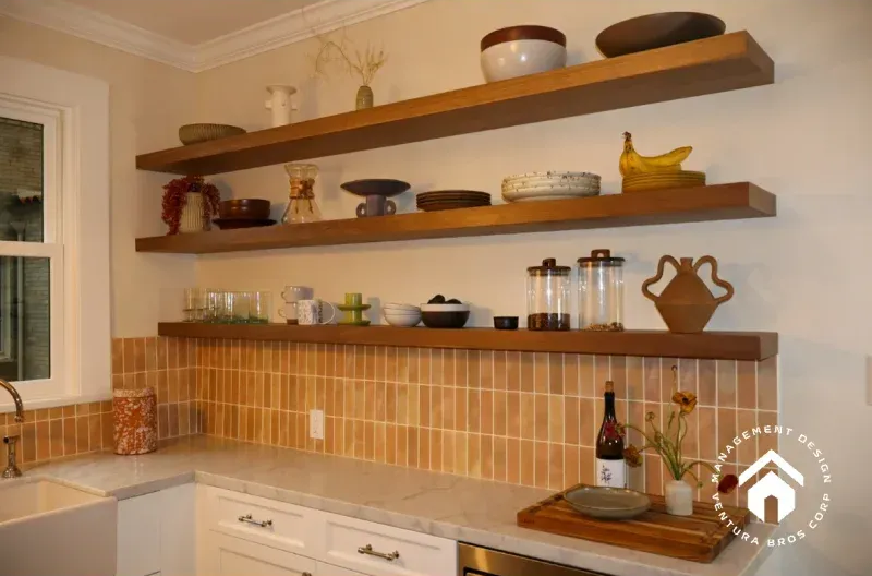 Three wooden floating shelves mounted on a light-colored kitchen wall above a tiled backsplash and white cabinets.