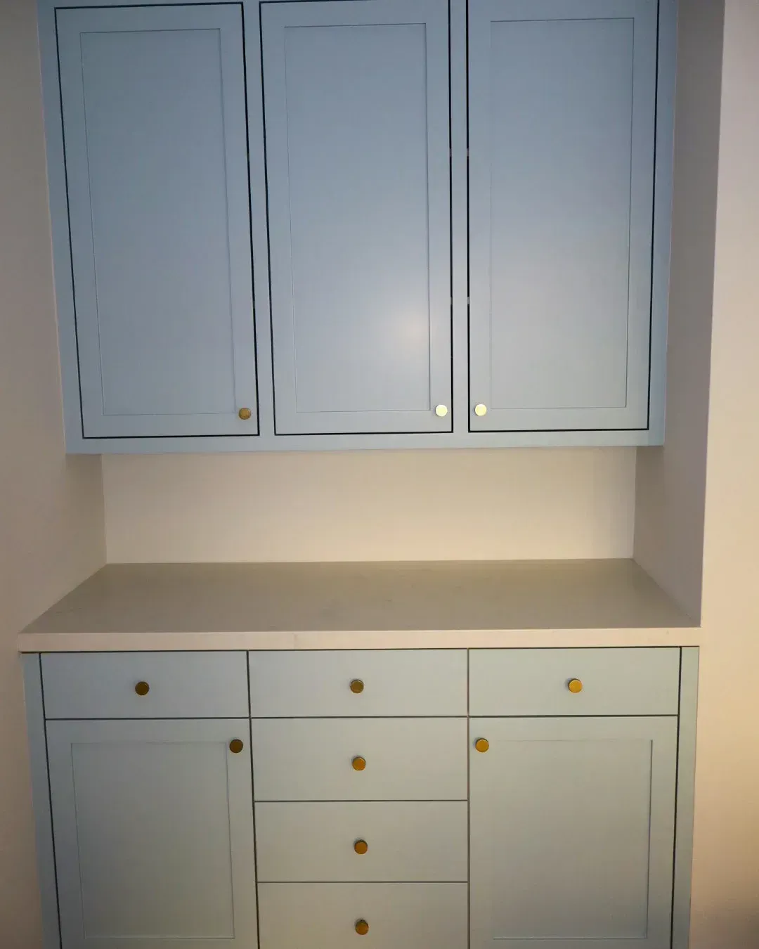 Light blue built-in cabinetry featuring upper cupboards and lower drawers with gold-toned circular knobs.