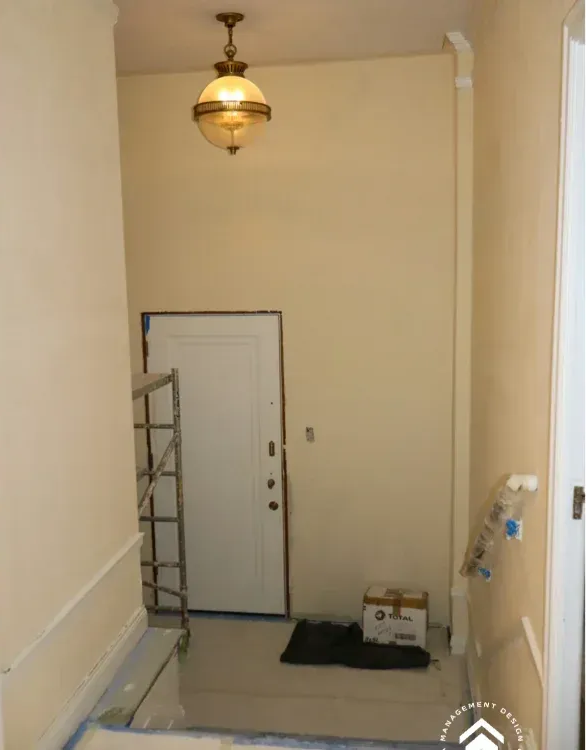 A beige interior entryway with a white door, a hanging globe lamp, a metal ladder, and a box on the floor.