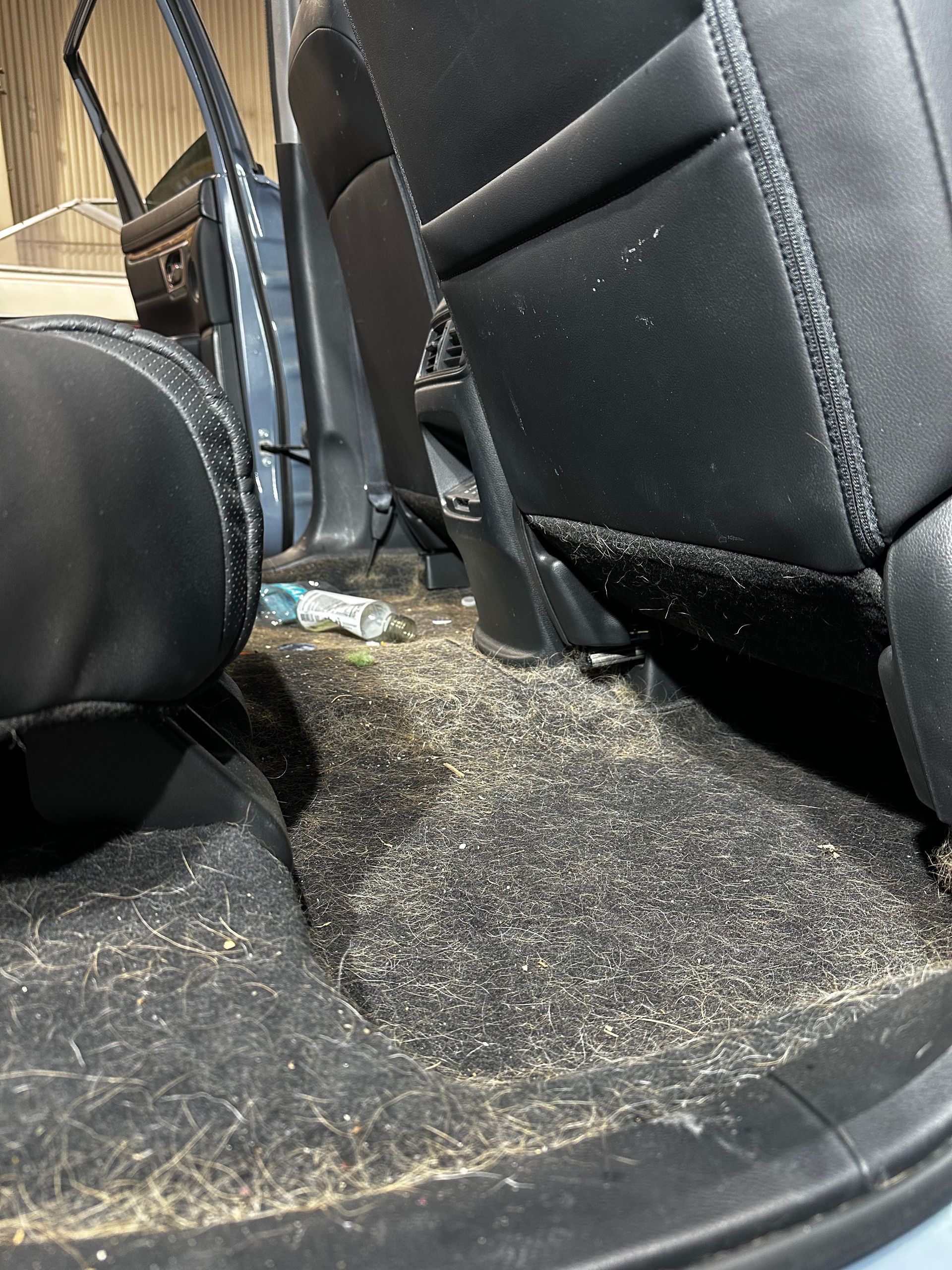 Car interior with black seats and dashboard, showing a dirty, debris-strewn floor and center console area