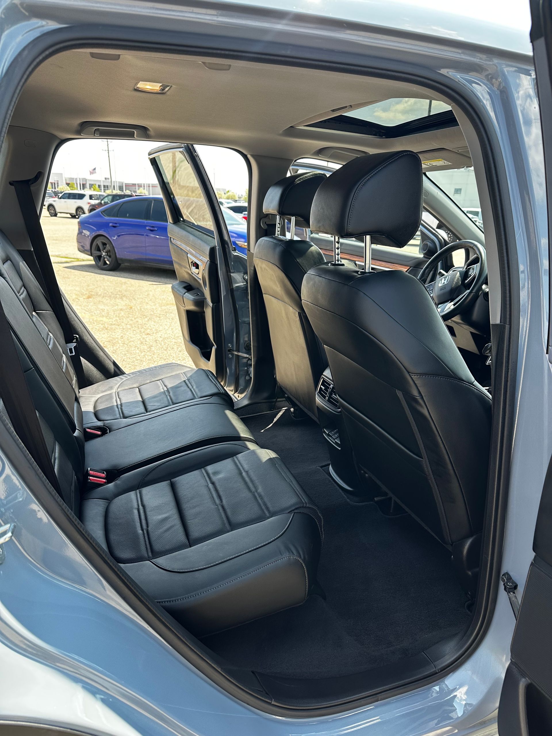Car interior with rear seat doors open, showing black leather seats and panoramic sunroof