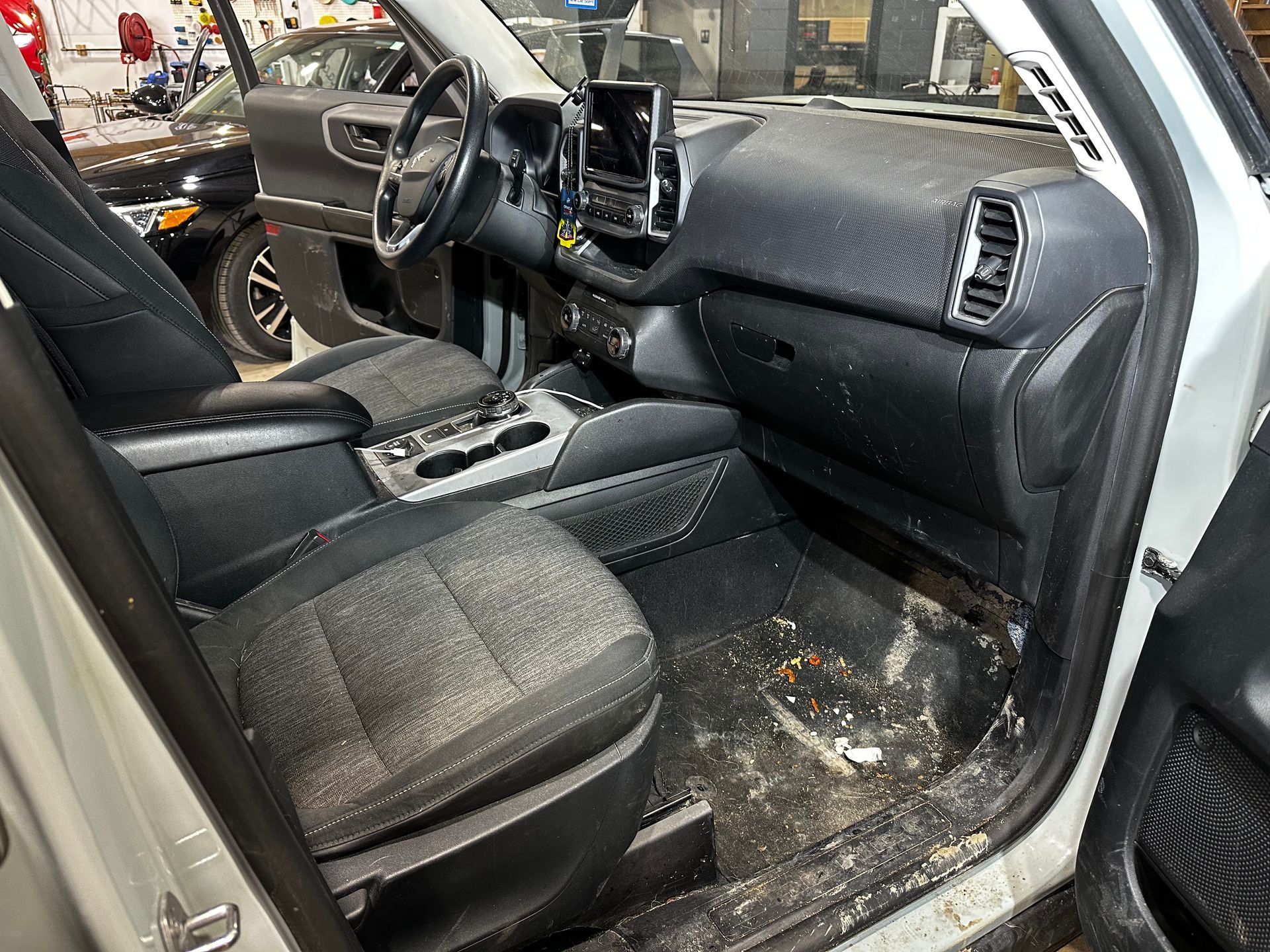 Car interior with black seats and dashboard, showing a dirty, debris-strewn floor and center console area