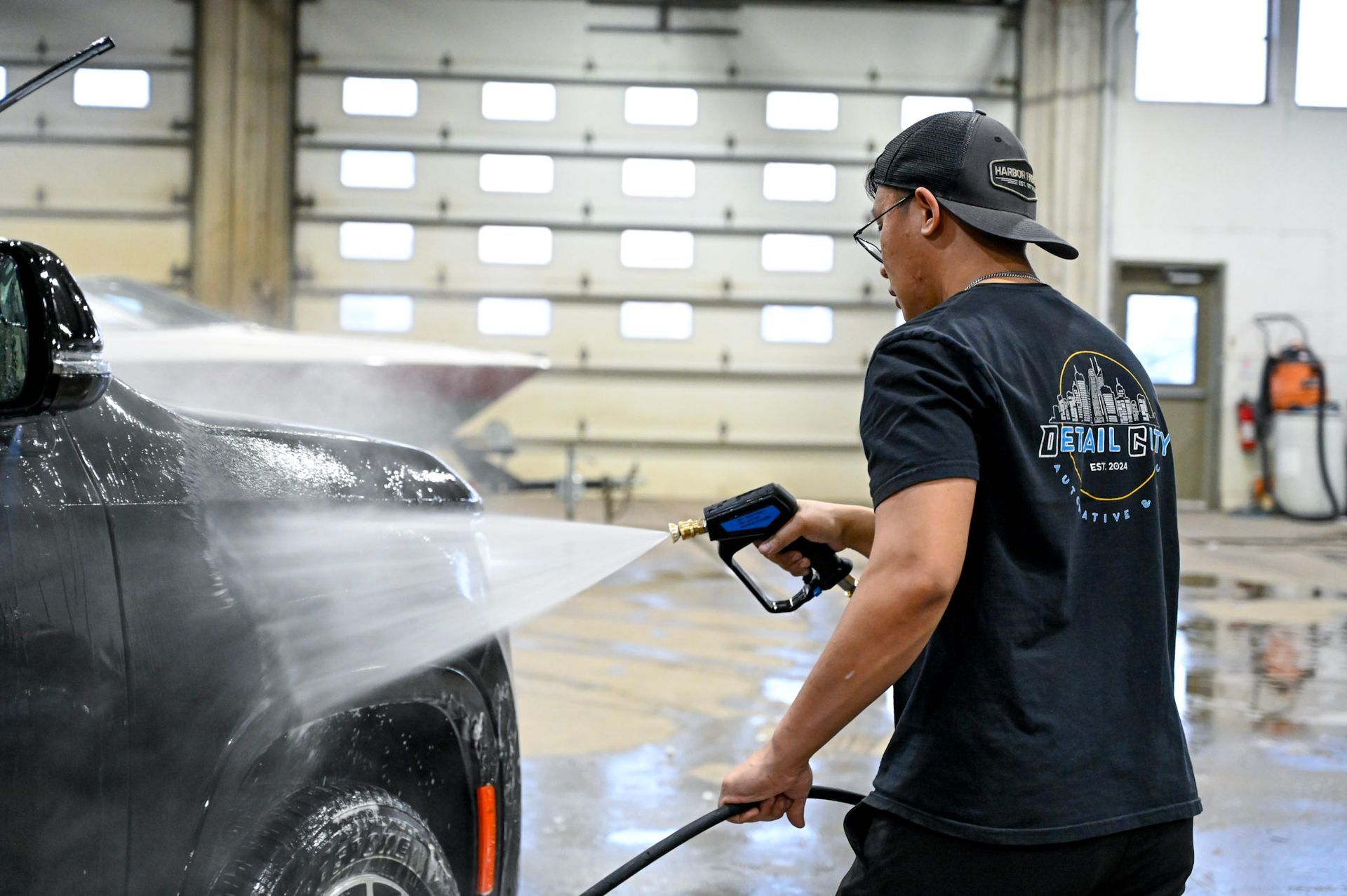 Person pressure-washing a black car in a garage with water spraying
