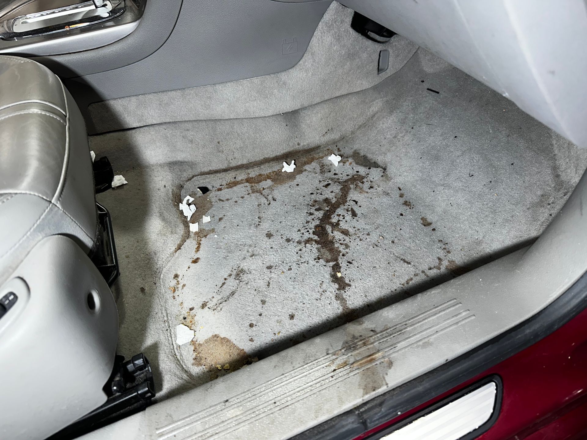 Car carpet with a large rust-colored stain and dirt near the passenger seat of a car