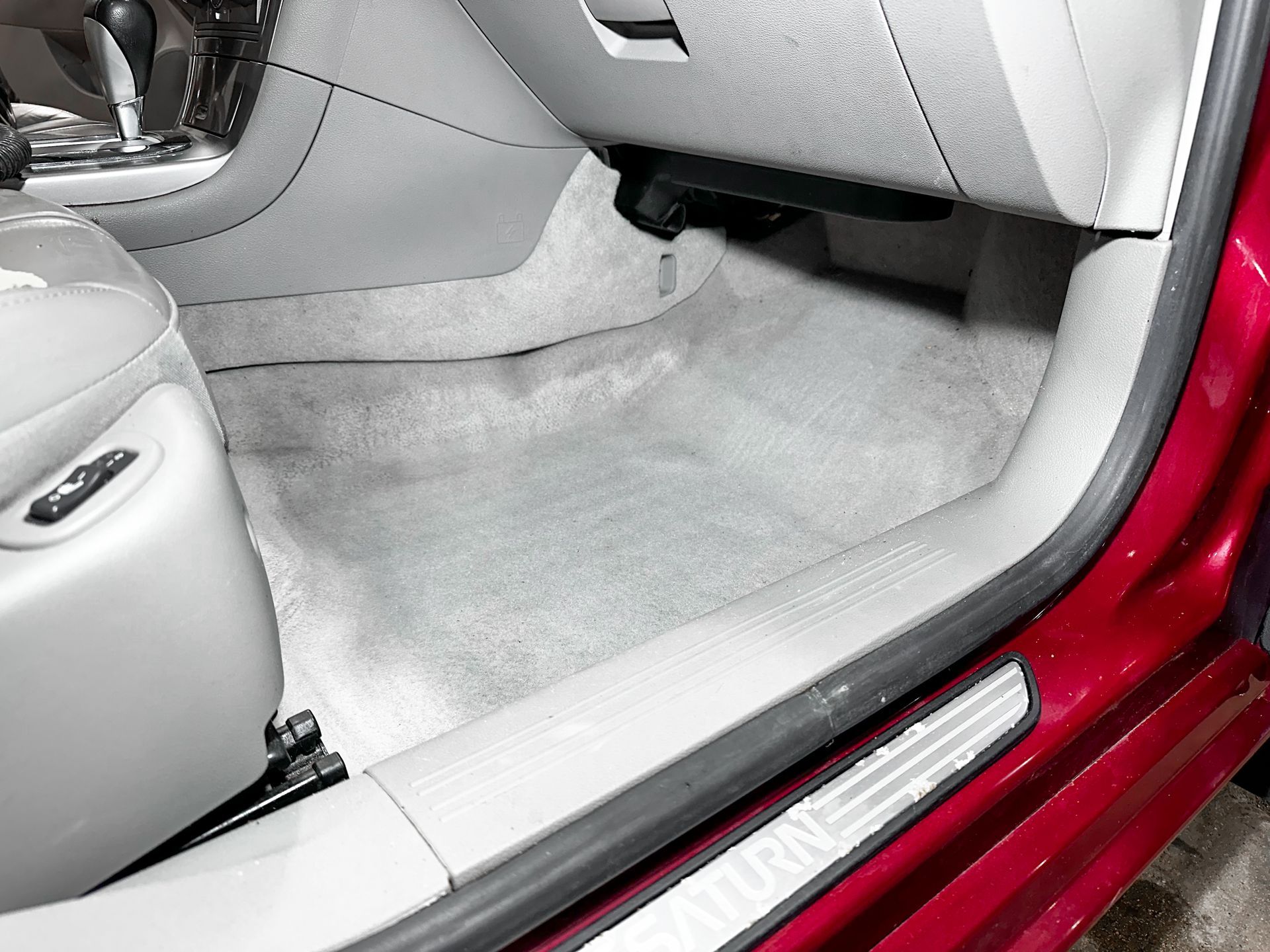 Car interior with gray floor mats and open red door sill, showing the front passenger footwell.