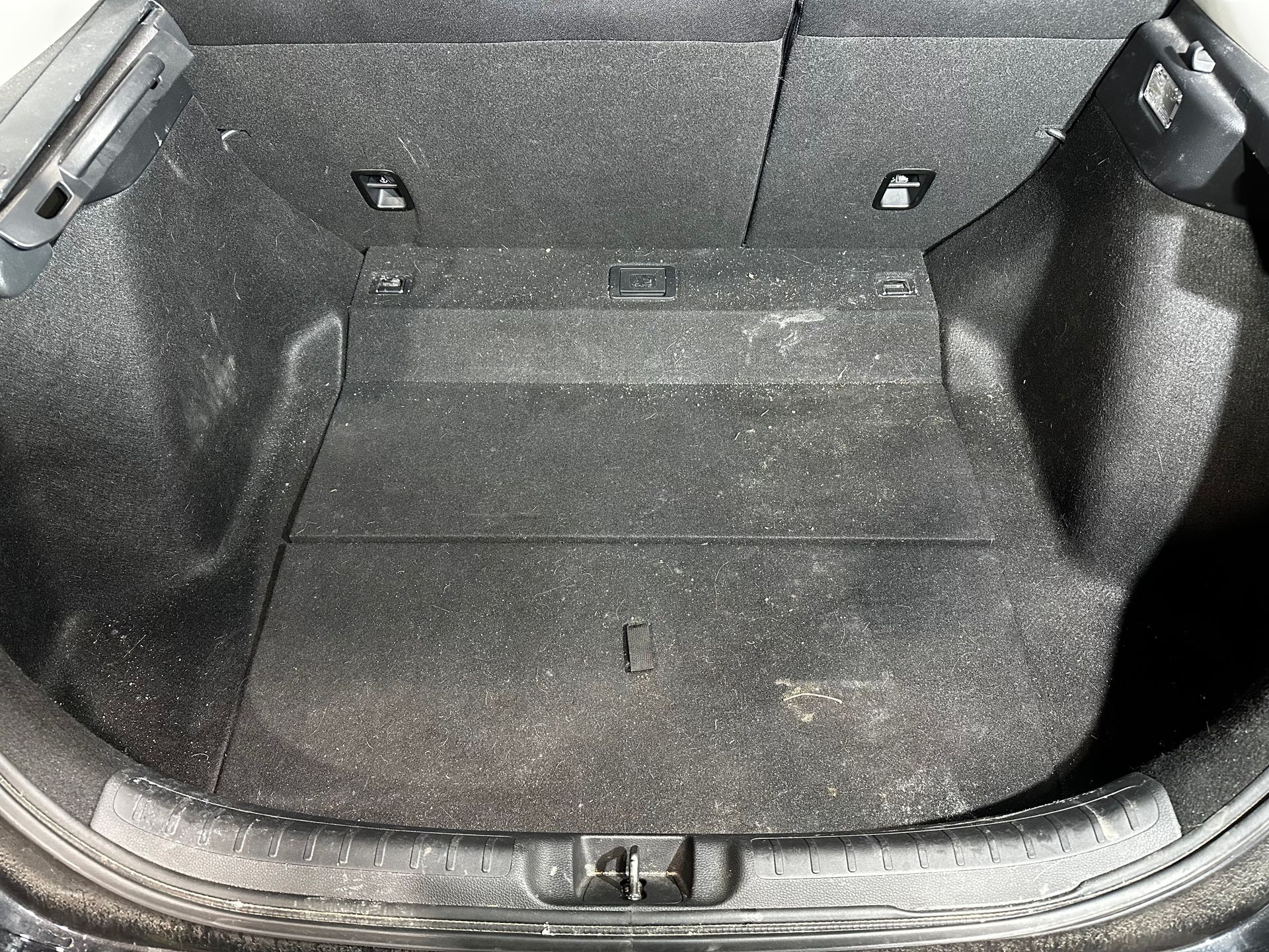 Empty car trunk with black carpeting and folded rear seats