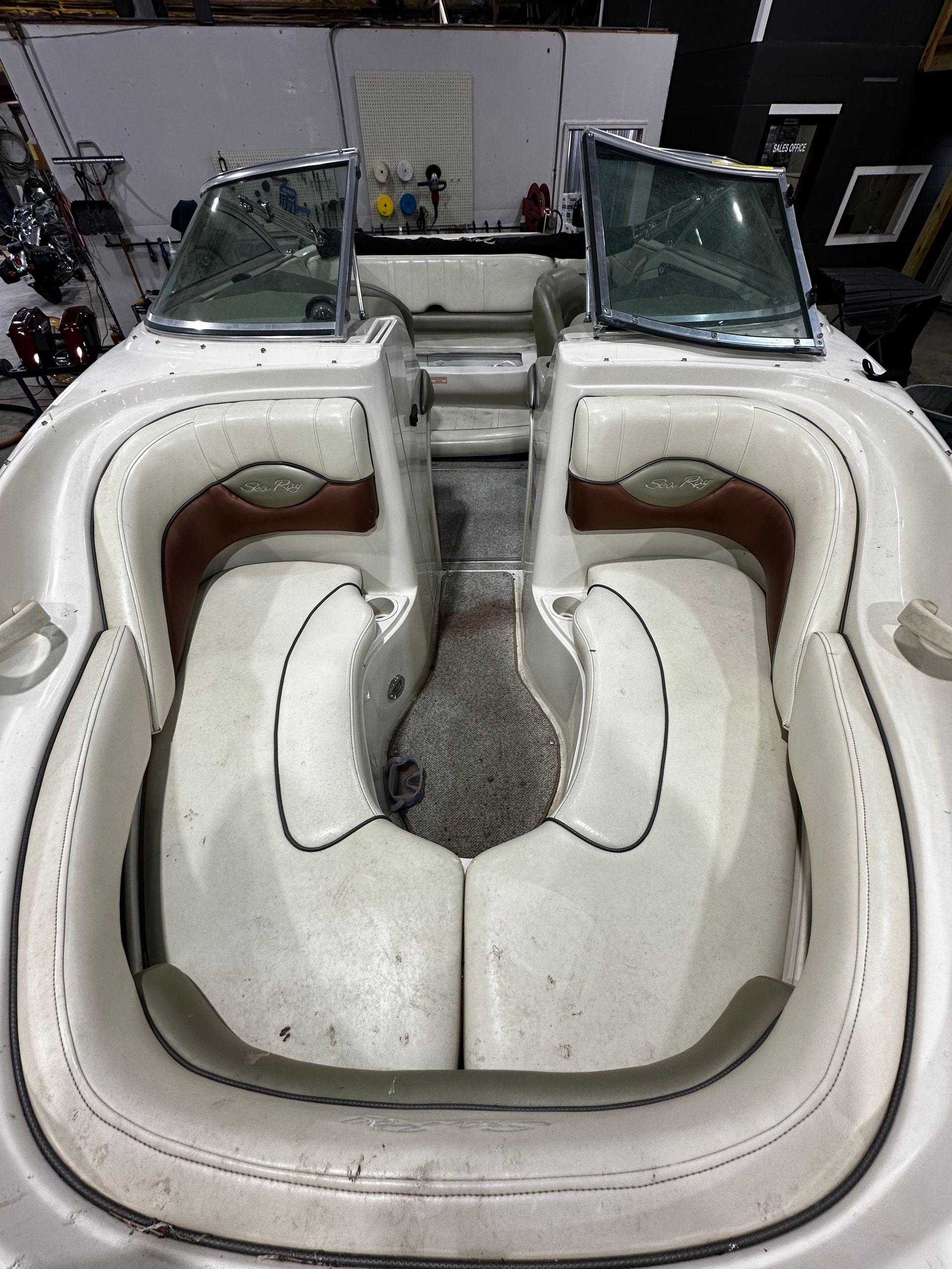 White boat interior with two front seats and a central walkway, shown in a workshop with the windshield open