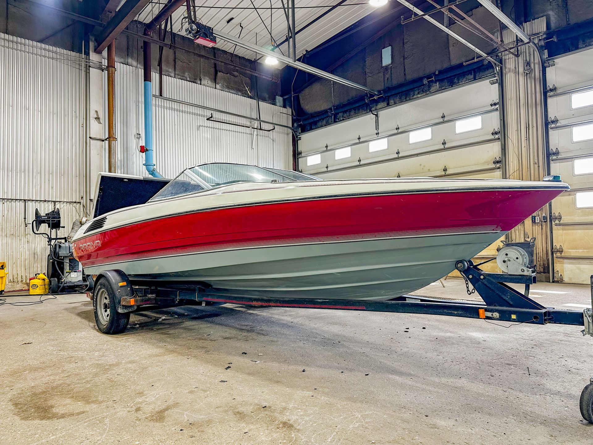 Speedboat with red, white, and silver hull on a trailer inside a boat repair warehouse.