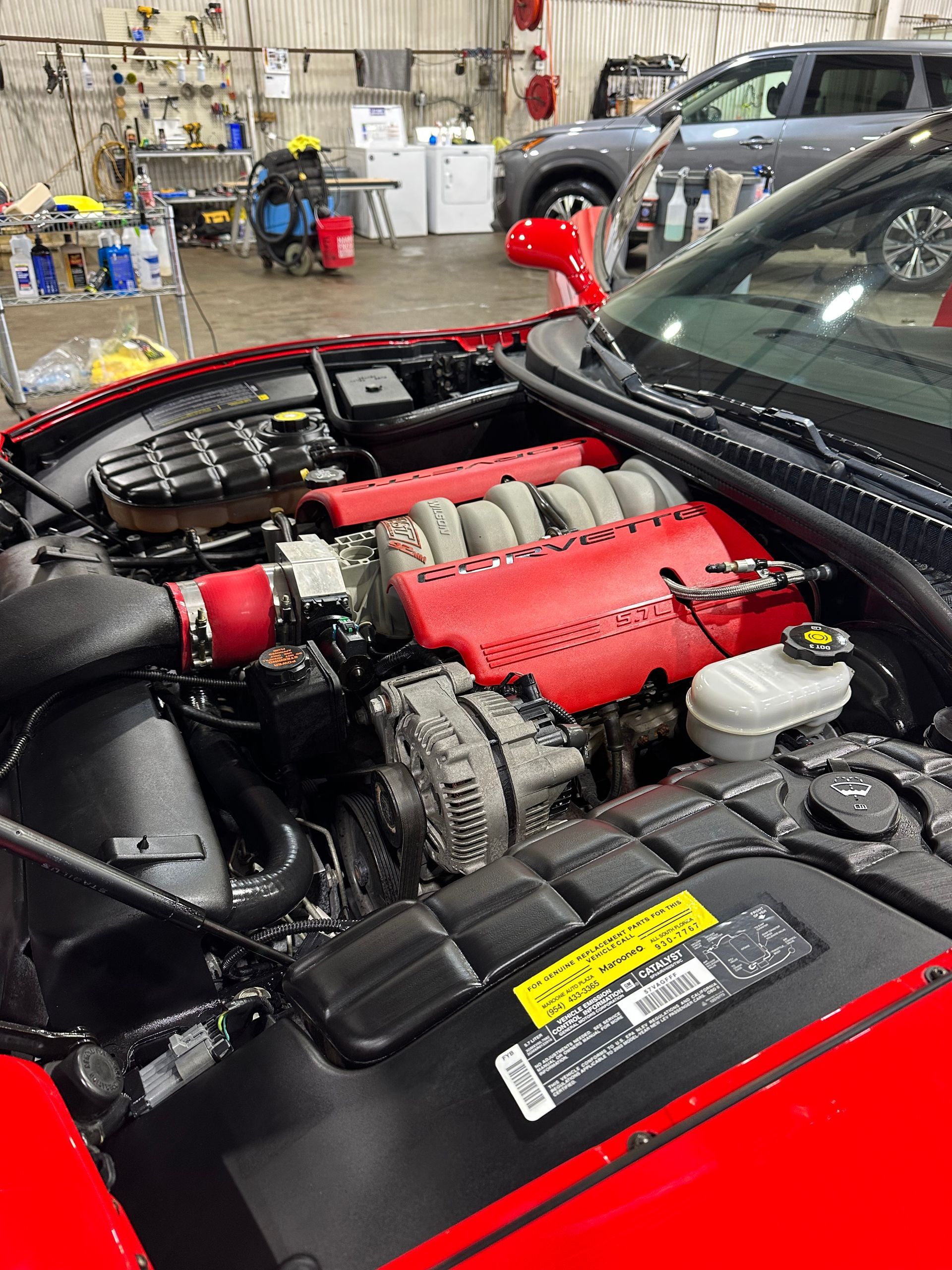 Red car engine bay with exposed engine and red intake components in a workshop